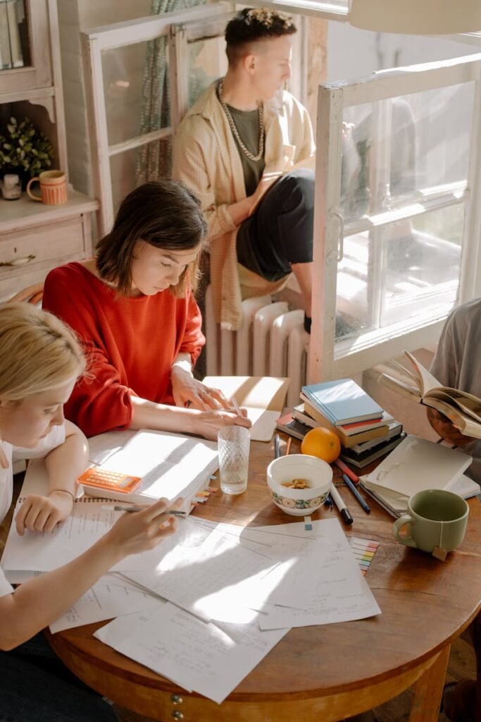 Group of college students studying in a sunlit room with books, papers, and a cozy atmosphere.